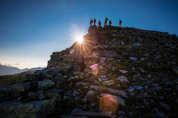 Menschen stehen auf einem Berggipfel und beobachten den Sonnenuntergang